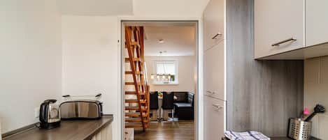 A modern kitchen with wooden flooring, a built-in stove, and a dining area with a chair and table.