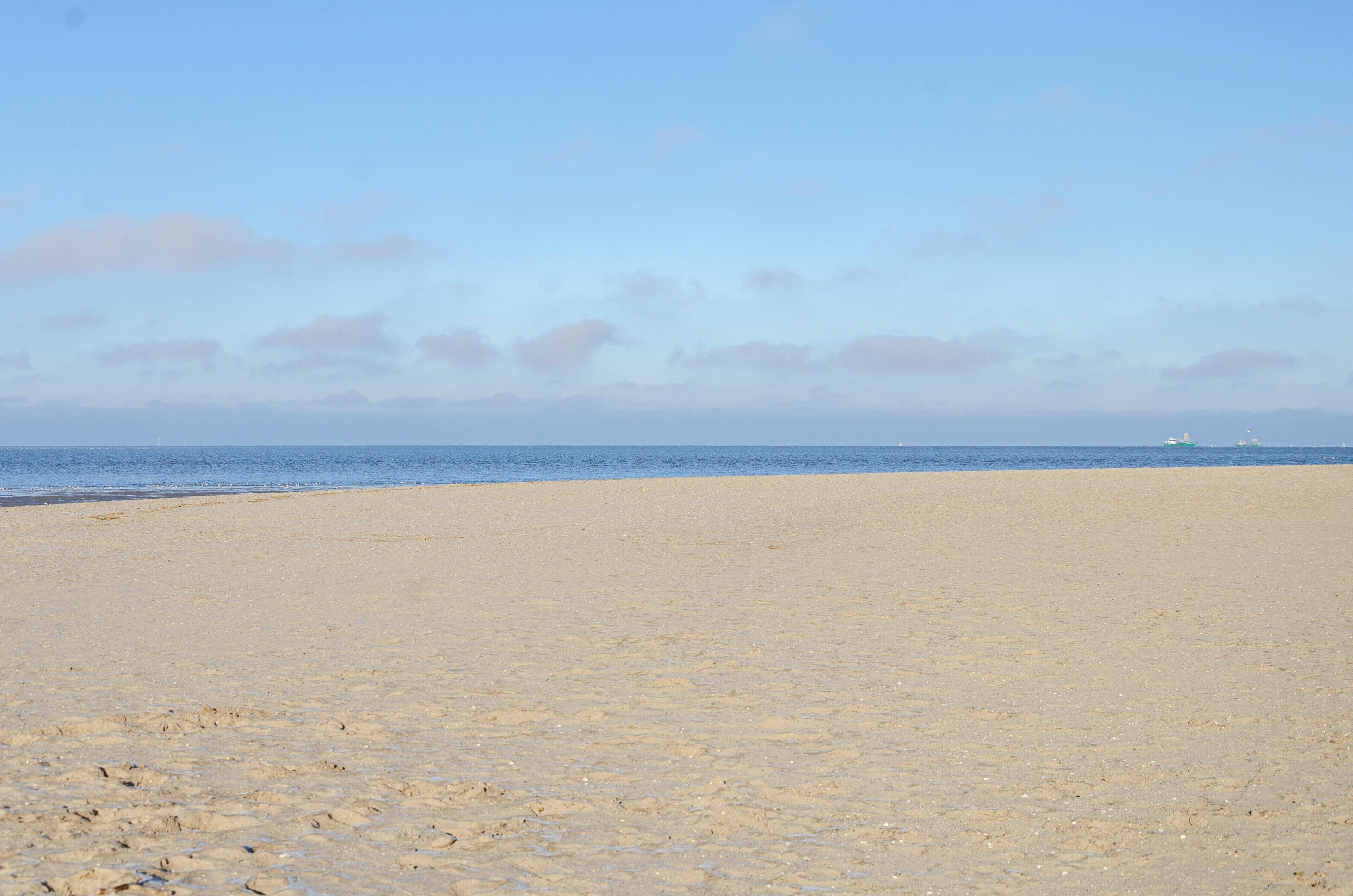 A wide sandy beach with a calm sea and a clear sky.
