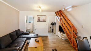 A living room with a sofa, a wooden table, a staircase, and a kitchen area. - Holiday Apartment "Nordsee 1" with Shared Terrace, Shared Garden & Wi-Fi (Wangerland)