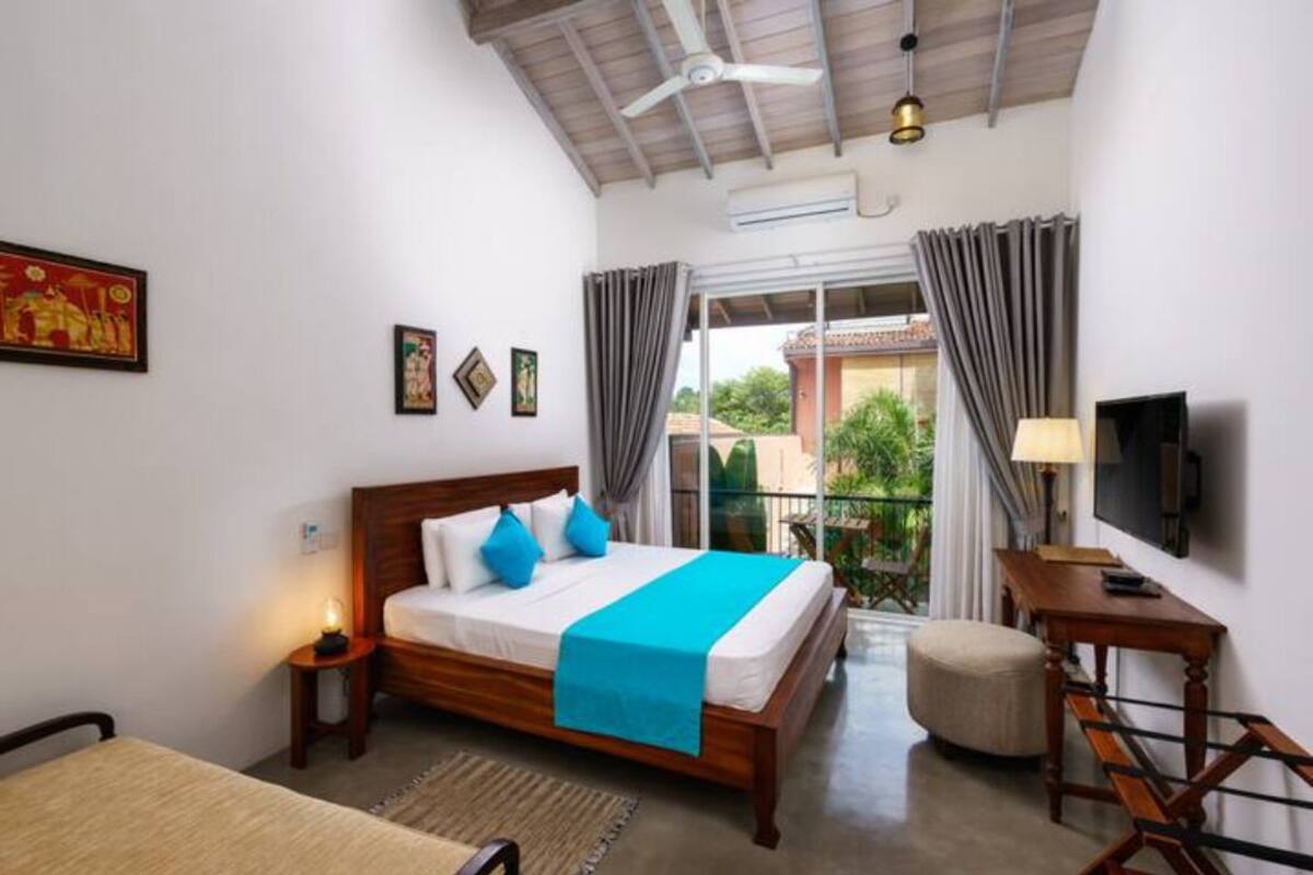 Ein Schlafzimmer mit einem Holzbett, einem kleinen Tisch, einem Stuhl, einem Fernseher und einem Balkon mit Vorhängen.