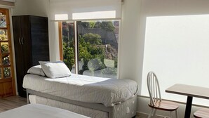 Un dormitorio con una cama grande, una cama más pequeña, un escritorio y una silla. Hay una ventana que ofrece vistas a zonas verdes.