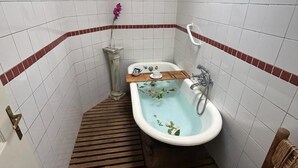 Un baño pequeño con bañera, un banco de madera, una toalla y un jarrón decorativo.
