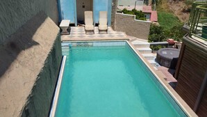 Una piscina rectangular con un diseño de cuadros a lo largo de los bordes, dos sillas de descanso y una mesita.