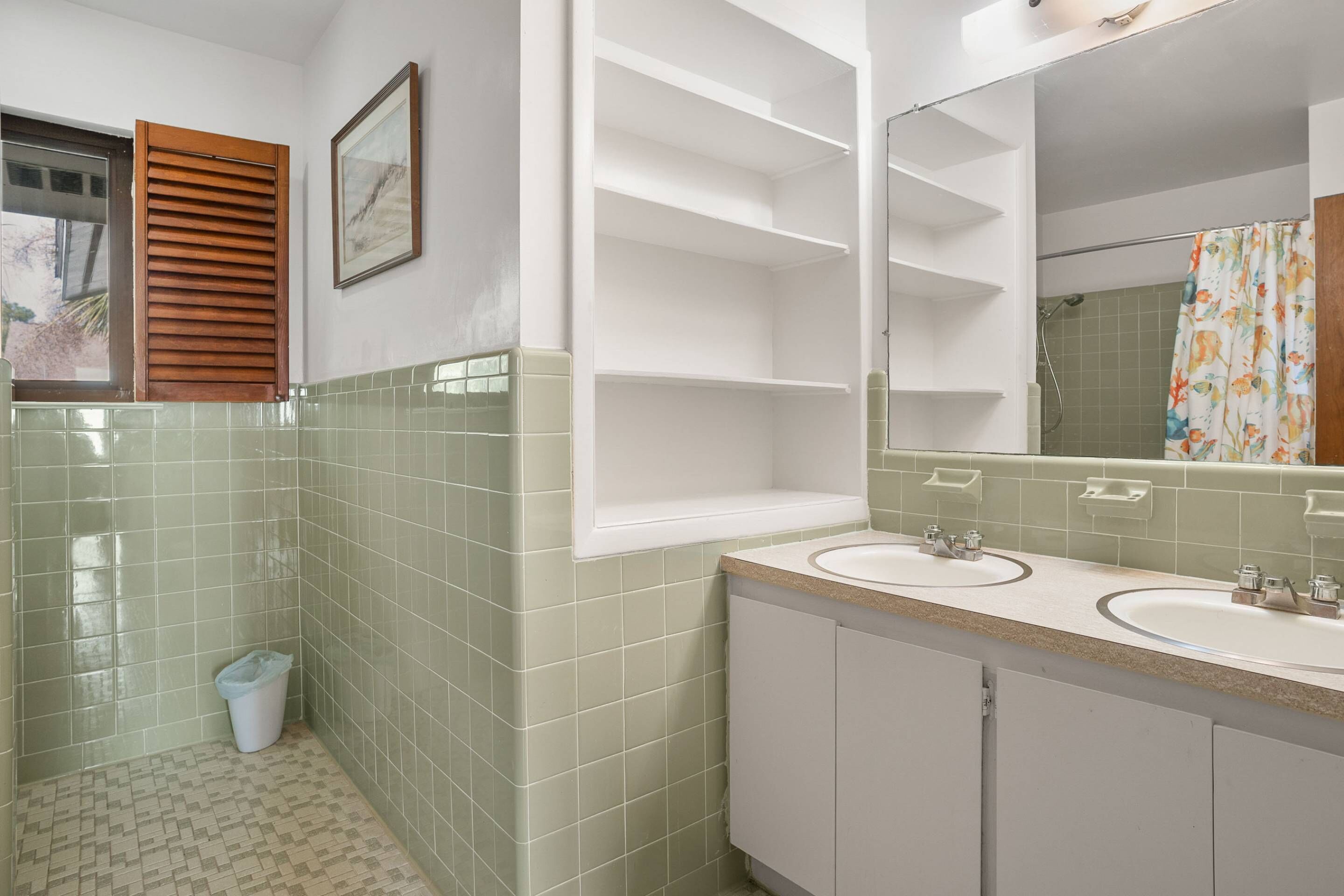 Une salle de bain avec deux lavabos, un miroir et une fenêtre avec des stores en bois.