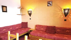 Een gezellige kamer met een rood gestreept bankje, twee houten stoelen, een klein tafeltje en wandlampen.