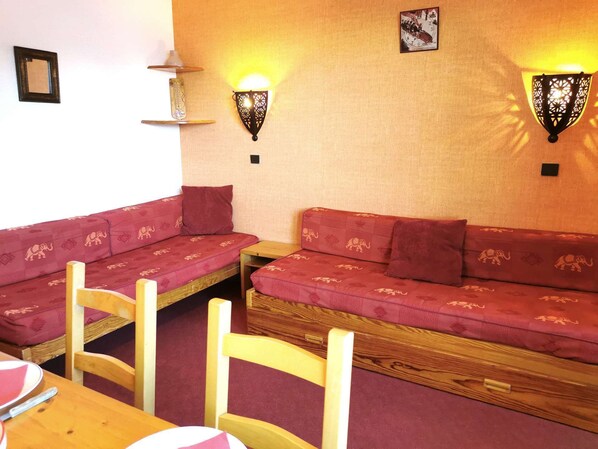 A cozy room with a red patterned sofa, two wooden chairs, a small table, and wall-mounted lamps. - Le Cristallin 41 - Charming 2-room apartment, close to the slopes (LES AVANCHERS VALMOREL)