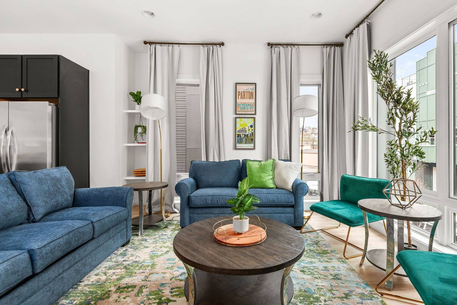Un soggiorno moderno con un divano blu, un tavolino rotondo e una poltrona verde. Si nota una libreria con piante e un quadro appeso al muro.