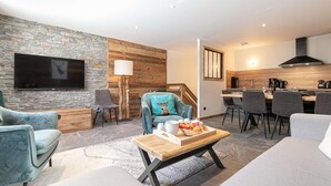 Een moderne woonkamer met een stenen muur, een flatscreen televisie en een eethoek met een houten tafel en stoelen.