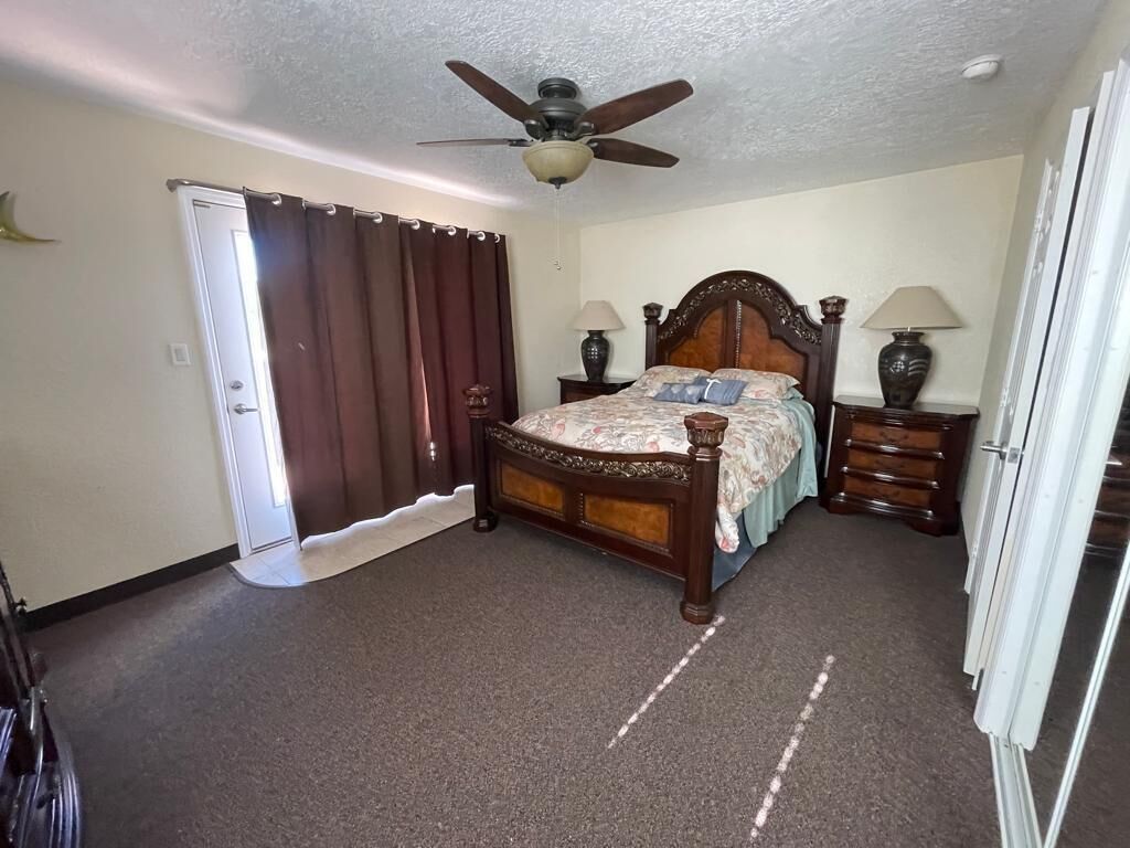 Une chambre à coucher avec un lit en bois, un ventilateur de plafond, deux tables de chevet avec des lampes et une porte avec des rideaux.