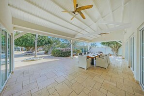 Une terrasse ouverte avec une table à manger, des chaises, des ventilateurs de plafond et une vue sur l’extérieur.