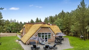 A thatched-roof building with a brick exterior, a patio with outdoor seating, and a surrounding forest. - "Aivars" -  from the sea by Interhome (Nørre Nebel)