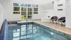 A modern indoor pool with clear glass walls, a view of the outdoors, and a seating area with chairs. - "Aivars" -  from the sea by Interhome (Nørre Nebel)