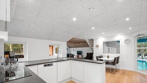 A modern kitchen with a large island, a dining area with a table and chairs, and a view of a swimming pool. - "Aivars" -  from the sea by Interhome (Nørre Nebel)