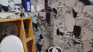 A bathroom with a wooden toilet seat, a bucket, and a marble-patterned wall. - Kasal's Stay (Kodaikanal)