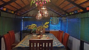 A dining area with a wooden ceiling, hanging flower decorations, and a table set with chairs. - Kasal's Stay (Kodaikanal)