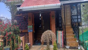 A house with a red-tiled roof, a wooden staircase, and a garden with plants and a hanging basket. - Kasal's Stay (Kodaikanal)