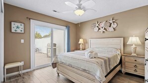 A bedroom with a bed, bedside tables, a ceiling fan, and a view through a sliding door to an outdoor area. - Salty Breeze Retreat With Pool & LSV By Beach Star (Myrtle Beach)