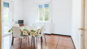 A dining area with a table set for four, white walls, a window with blinds, and a tiled floor. - Appartamento Sauro: A cozy apartment situated a few minutes from the town center, with Free WI-FI. (Rapallo)