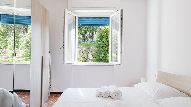 A bedroom with a bed, a window with a view of greenery, and a door leading to another room. - Appartamento Sauro: A cozy apartment situated a few minutes from the town center, with Free WI-FI. (Rapallo)