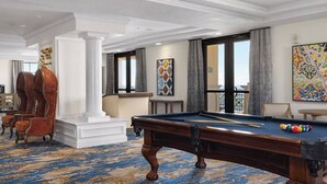 Amplia habitación con mesa de billar, asientos cómodos y grandes ventanales con vistas.