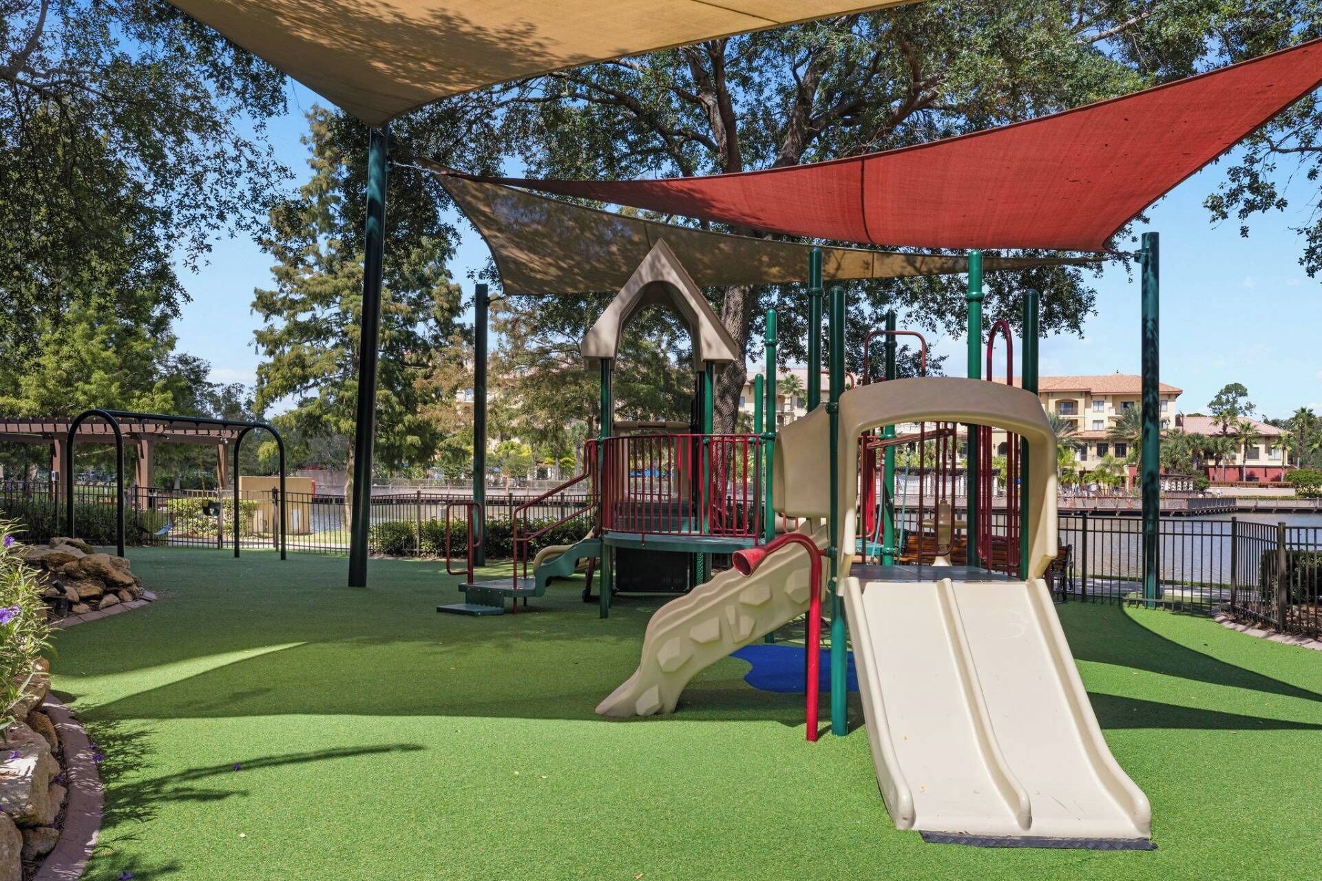 Un parque infantil con tobogán, estructuras para escalar y una zona sombreada.