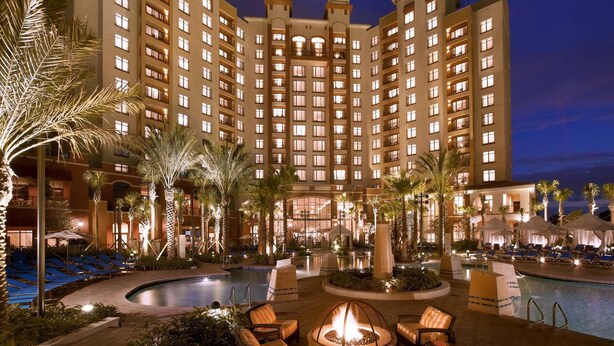 Un hotel su più piani con area piscina, posti a sedere all'aperto e palme.