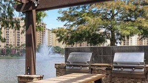 Patio esterno con due barbecue, un tavolo in pietra e una fontana sullo sfondo.