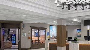 Una hall d'albergo con una reception, una macchina da caffè Starbucks e un'ampia finestra con vista sulla città.