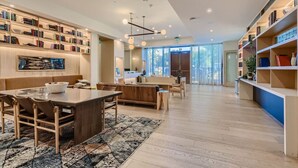 A spacious living area with a wooden dining table, a sofa, and a bookshelf filled with books. - Luxury 1BR +Views+Rooftop Pool +Walk To Rainey St. (Austin)