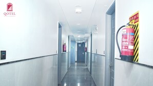 Un pasillo de hotel con un extintor a la derecha, un cartel en la pared y una puerta al final.