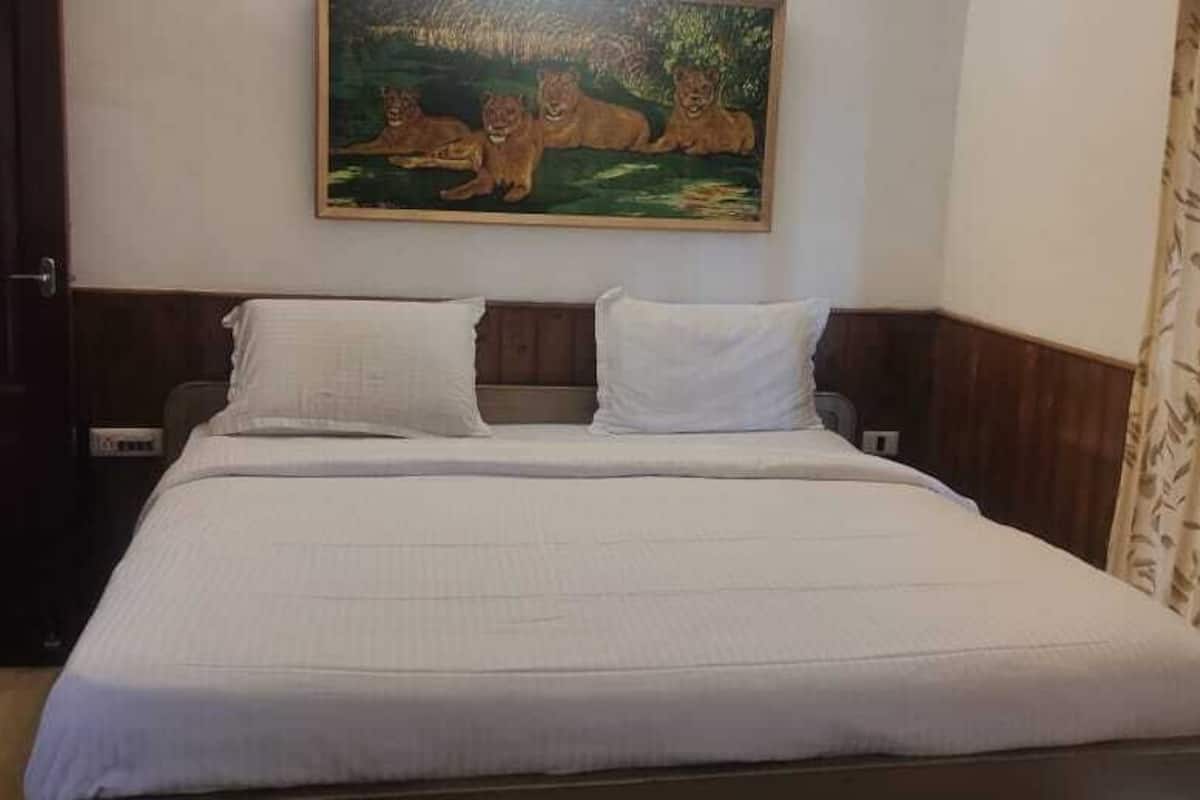 A neatly made bed with white linens, a painting of lions on the wall above, and a wooden door to the left.