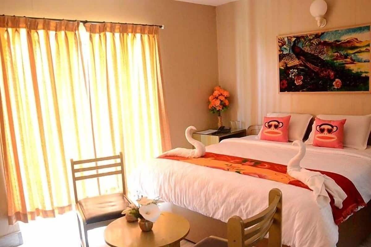 A hotel room with a bed, a chair, a small table, and a painting on the wall.