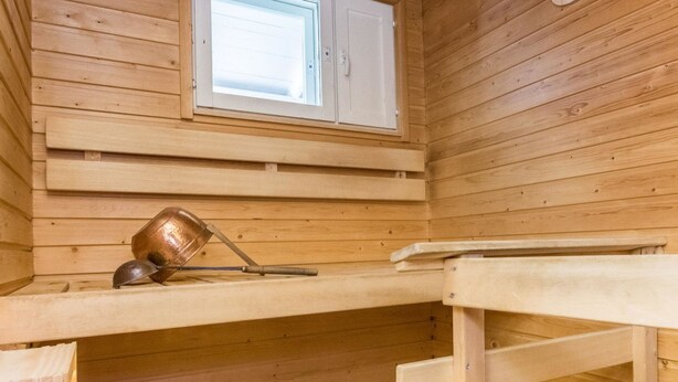 Un sauna avec des murs en bois, une fenêtre, un banc et un seau en métal.