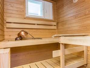 Uma sala de sauna com paredes de madeira, uma janela, um banco e um balde de metal.