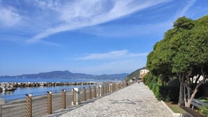 A paved walkway with a mosaic pattern, bordered by a wooden fence and trees, leading to a body of water with mountains in the background. - Apartment Enrico by Interhome (Chiavari)