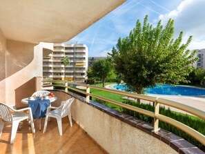 A balcony with a table and chairs, overlooking a swimming pool and a tree.