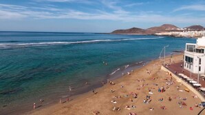 Uma praia com águas azuis cristalinas, pessoas se banhando ao sol, e edifícios ao fundo.