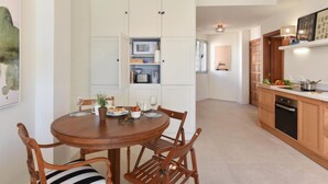 Uma cozinha moderna com armários brancos, uma área de refeições com uma mesa redonda de madeira e vista para a sala de estar.