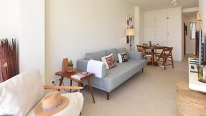 Uma sala de estar com um sofá cinzento, uma pequena mesa lateral de madeira, um chapéu e um abajur.