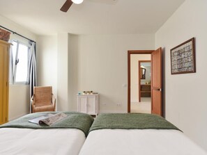 Een slaapkamer met twee bedden, een stoel, een klein kastje en een deur naar een andere kamer.