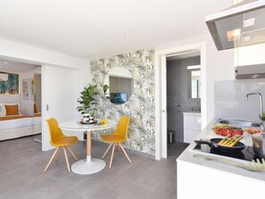 A modern kitchen with a white countertop, a sink, and a stove. There is a dining area with a round table and two yellow chairs.