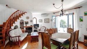 Ein großzügiges Wohnzimmer mit einer Holztreppe, einem Essbereich mit Tisch und Stühlen, einem Kamin und einem Fernseher.