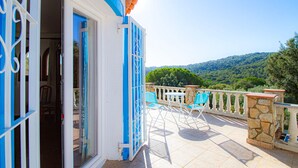 Ein Balkon mit Steinbalustrade, Blick auf eine gebirgige Landschaft und ein blauer Stuhl.