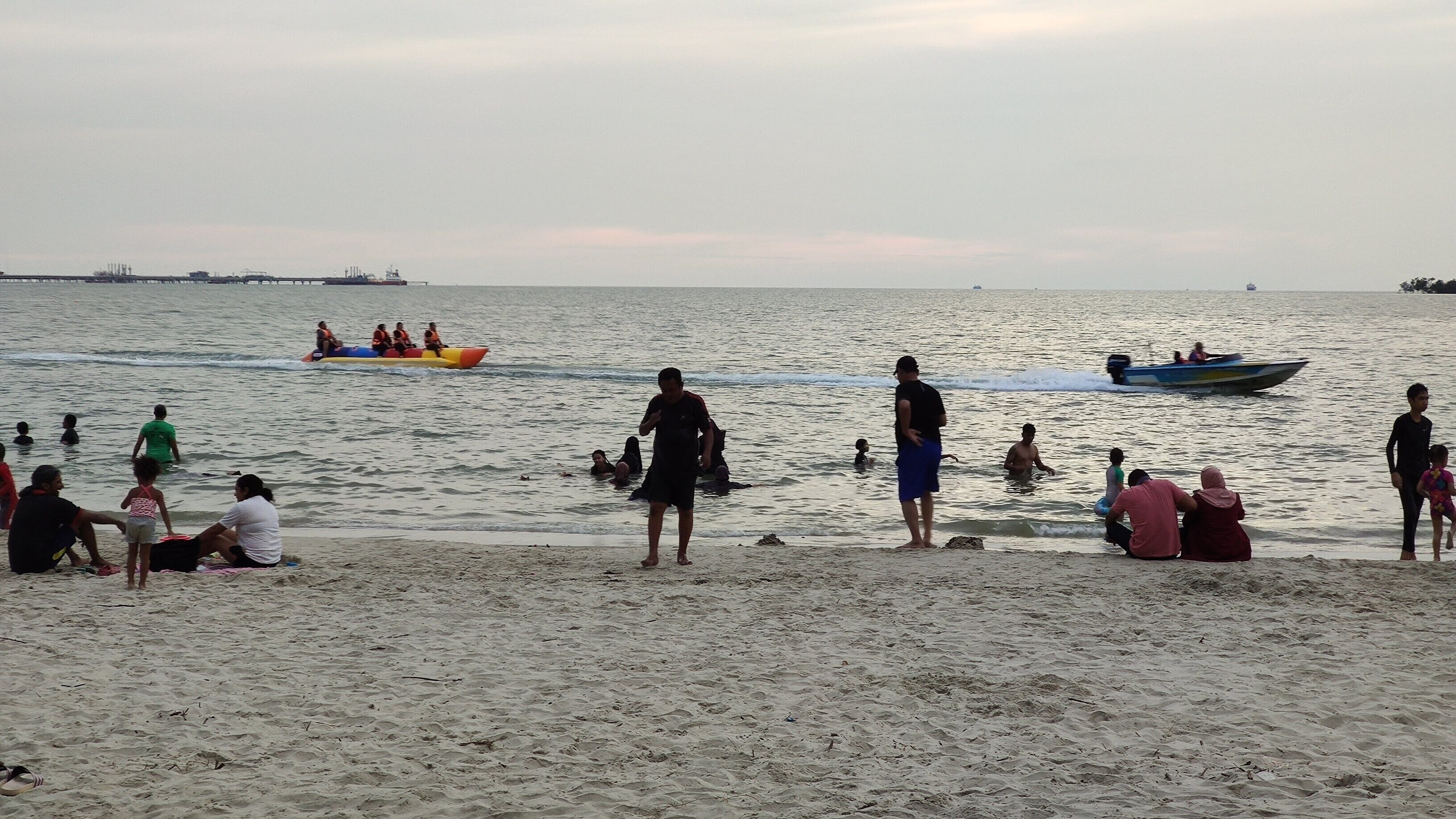 A beach with people swimming and boats in the water.