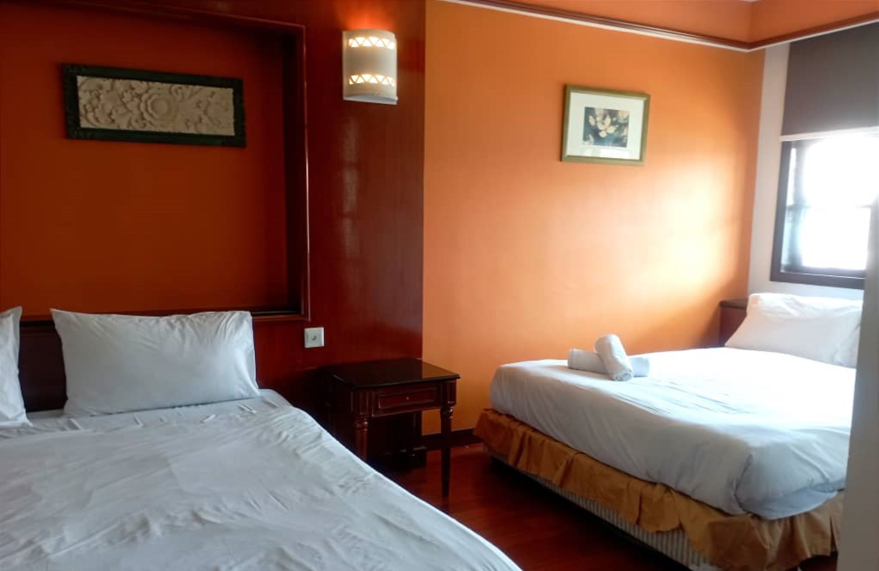 Een hotelkamer met twee bedden, een nachtkastje, een wandlamp en een raam.