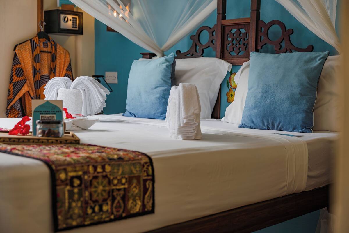 Una cama bien hecha con sábanas blancas, almohadas azules y un cabecero decorativo.