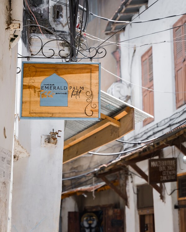 A wooden sign with the text "Zanzibar Emerald Palm Boutique hotel" hanging from a building.