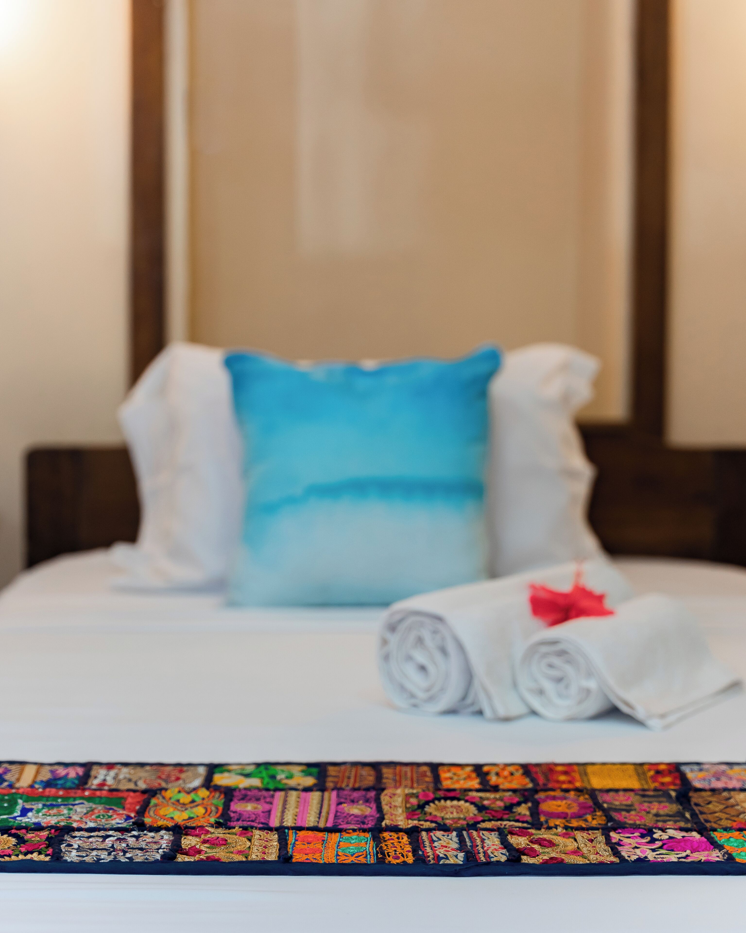A bed with a blue pillow, white pillows, and a rolled white towel with a red bow.