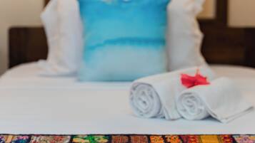 A bed with a blue pillow, white pillows, and a rolled white towel with a red bow.