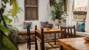 A cozy room with a wooden table, a bench with colorful cushions, and a potted plant. - Emerald Palm Boutique Hotel (Zanzibar Town)